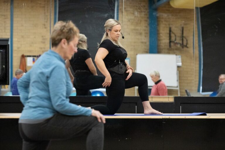 An instructor doing yoga in a gym with another person in the background